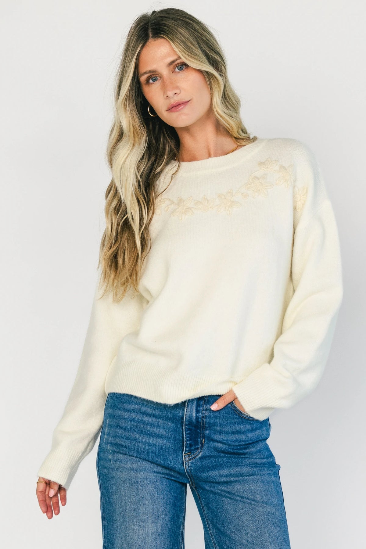 Model wearing a cream knit sweater with a round neckline, long sleeves, and ribbed trim. The sweater features tonal floral appliqué detailing throughout and a relaxed silhouette for a cozy, feminine look.