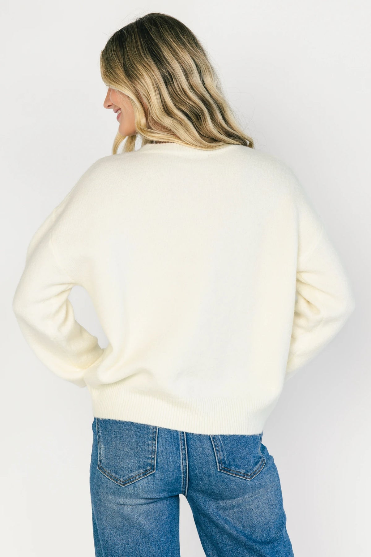 Model wearing a cream knit sweater with a round neckline, long sleeves, and ribbed trim. The sweater features tonal floral appliqué detailing throughout and a relaxed silhouette for a cozy, feminine look.