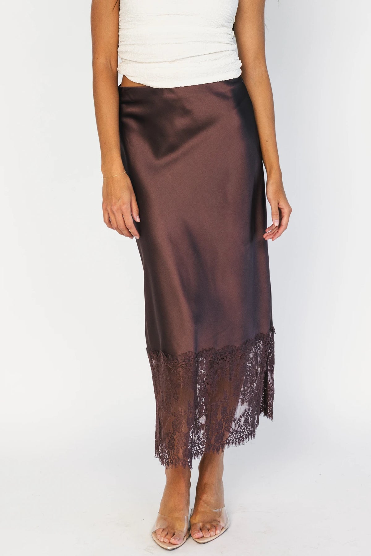 Model wearing the Kamara Satin Lace Skirt in Chocolate featuring a high-rise waistband, bias-cut satin silhouette, delicate floral lace trim at the hem, and a flowing midi length.