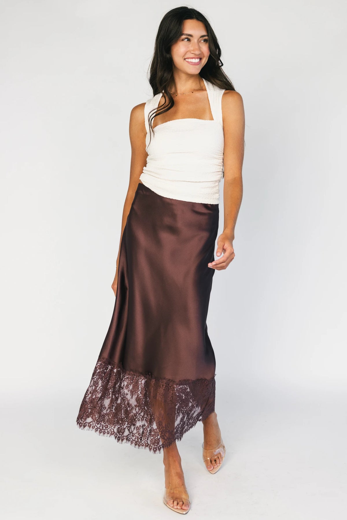 Model wearing the Kamara Satin Lace Skirt in Chocolate featuring a high-rise waistband, bias-cut satin silhouette, delicate floral lace trim at the hem, and a flowing midi length.