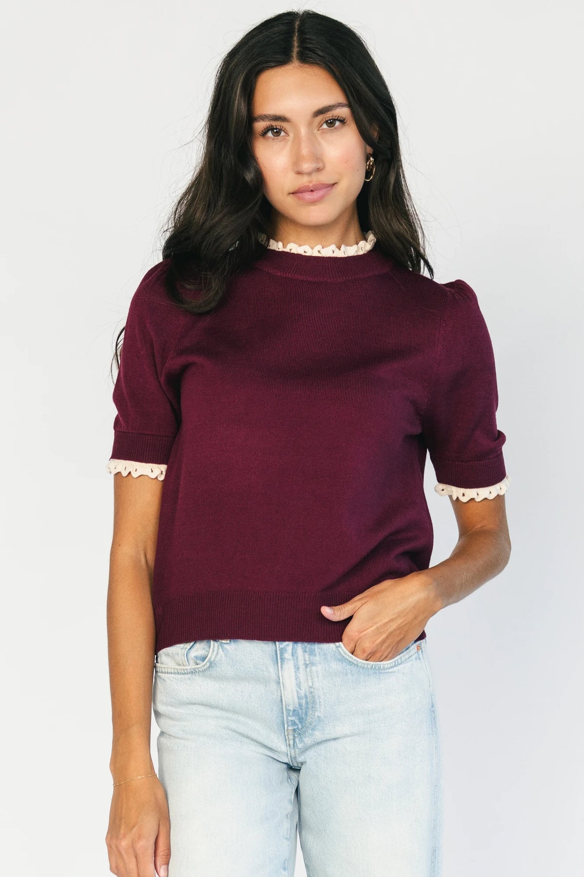 Model wearing the Adeline Sweater Top in Wine featuring a mock neckline, short sleeves with gathered shoulders, contrast ivory eyelet ruffle trim at the neckline and cuffs, and a classic fitted knit silhouette.