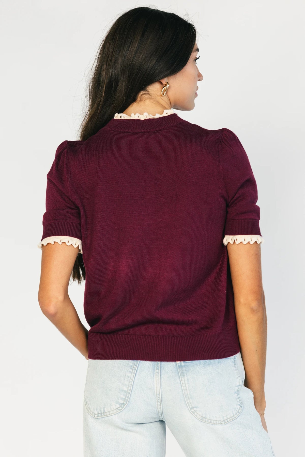Model wearing the Adeline Sweater Top in Wine featuring a mock neckline, short sleeves with gathered shoulders, contrast ivory eyelet ruffle trim at the neckline and cuffs, and a classic fitted knit silhouette.