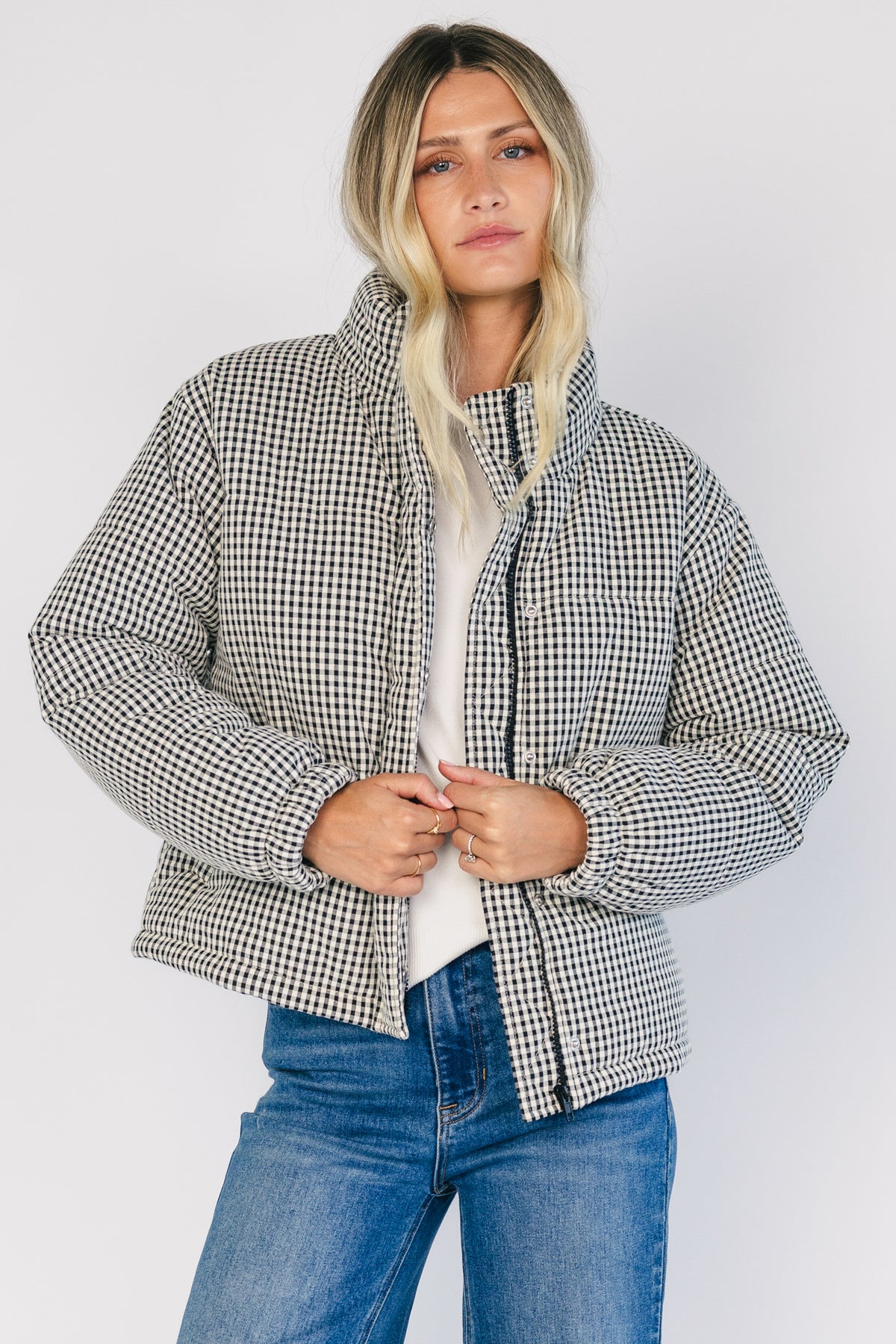 Model wearing the Vivienne Coat featuring a black and white gingham quilted puffer design with a high collar, front zipper and snap-button closure, long sleeves, and a relaxed silhouette.