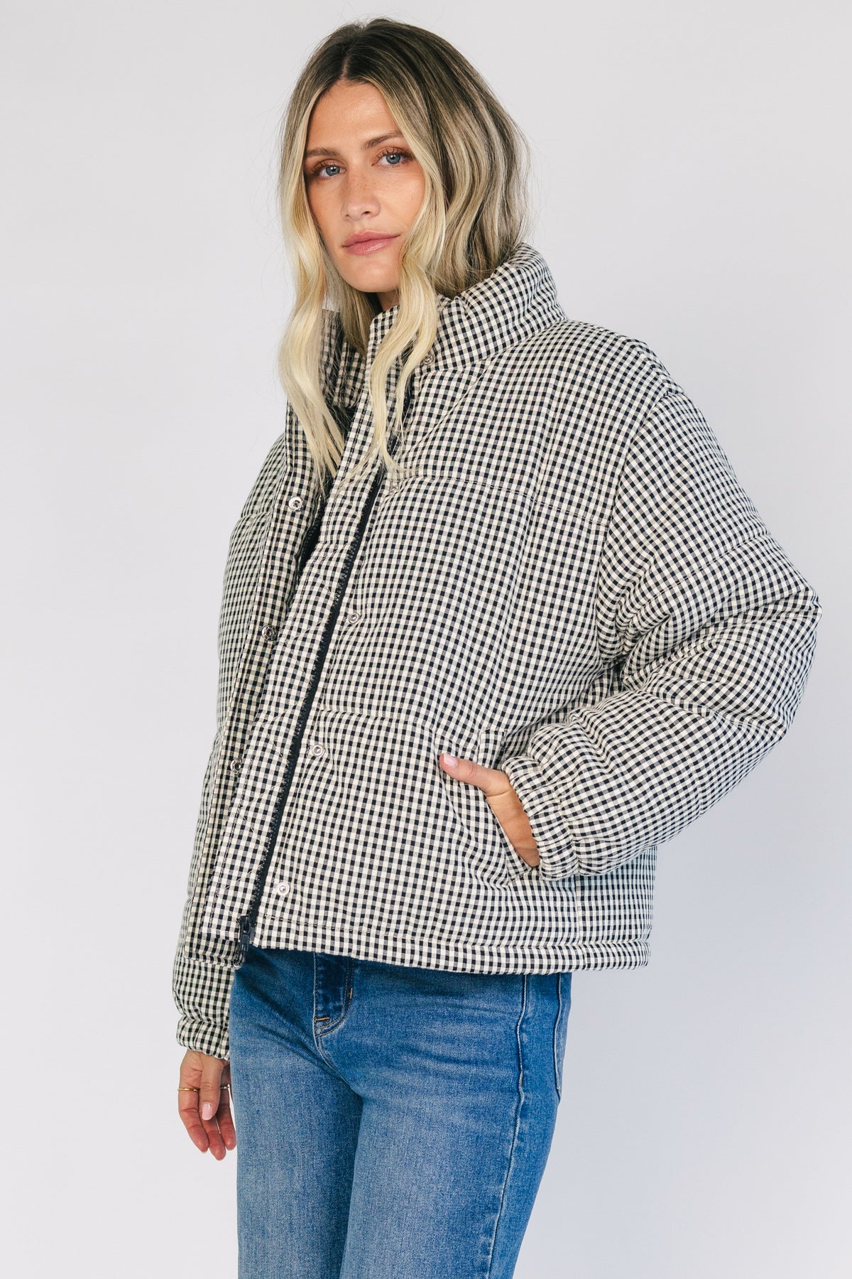 Model wearing the Vivienne Coat featuring a black and white gingham quilted puffer design with a high collar, front zipper and snap-button closure, long sleeves, and a relaxed silhouette.