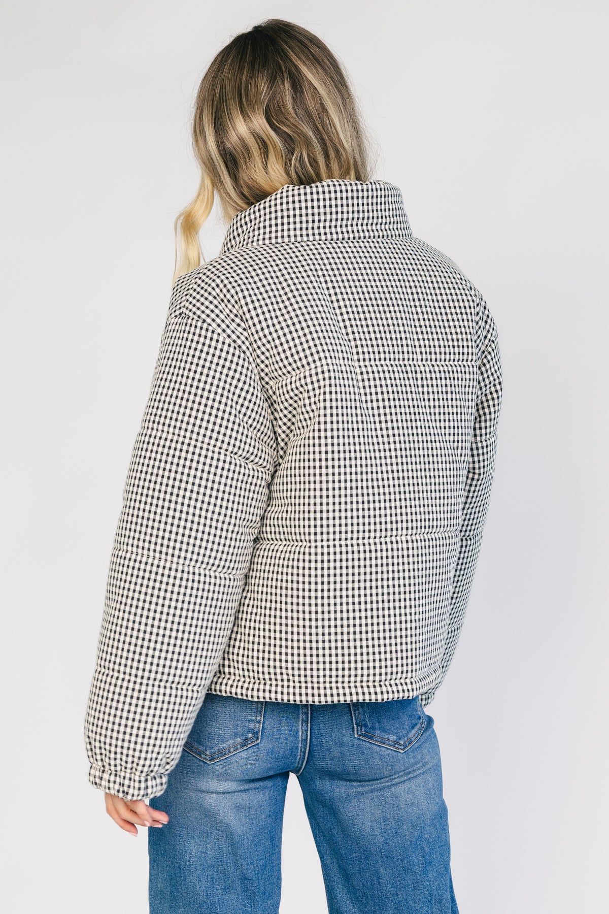 Model wearing the Vivienne Coat featuring a black and white gingham quilted puffer design with a high collar, front zipper and snap-button closure, long sleeves, and a relaxed silhouette.