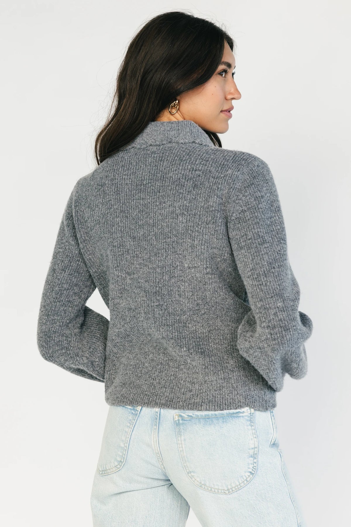 Model wearing a gray knit cardigan with a scalloped collar, adjustable black velvet bow detail, two front hook-and-eye closures, and a relaxed fit.