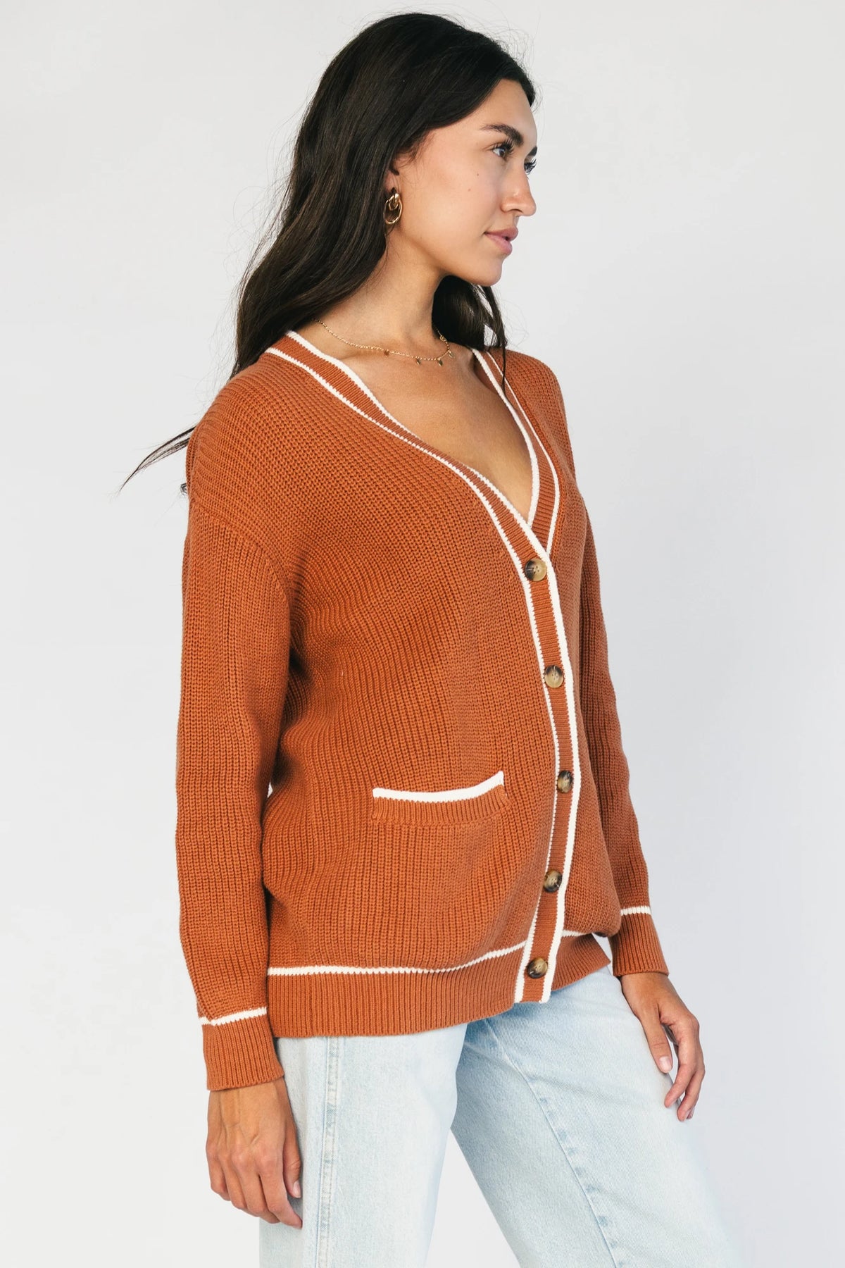 Model wearing a spice orange chunky knit cardigan with a V-neckline, five-button front closure, long sleeves, ribbed trim, front patch pockets, and a relaxed oversized fit.