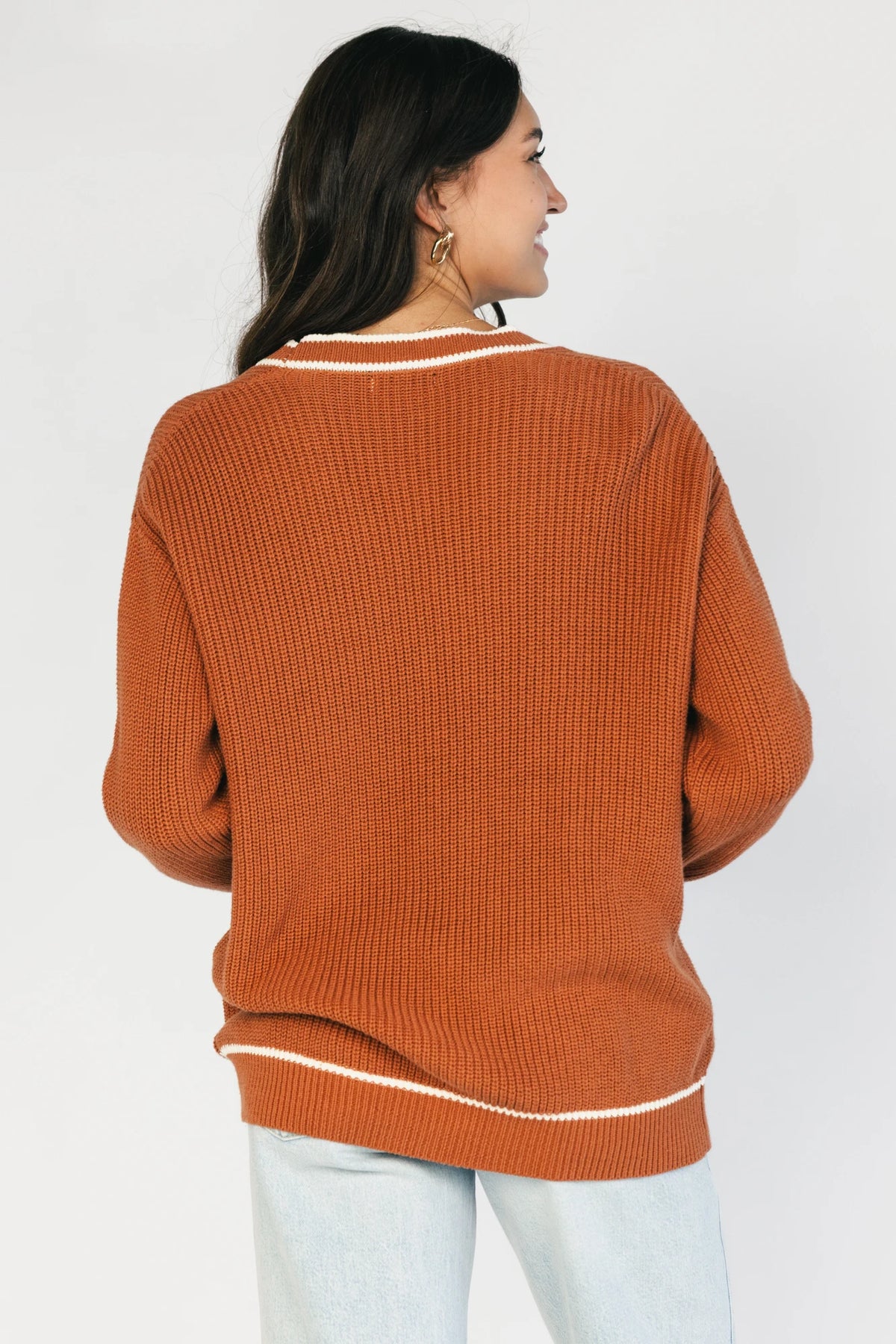 Model wearing a spice orange chunky knit cardigan with a V-neckline, five-button front closure, long sleeves, ribbed trim, front patch pockets, and a relaxed oversized fit.