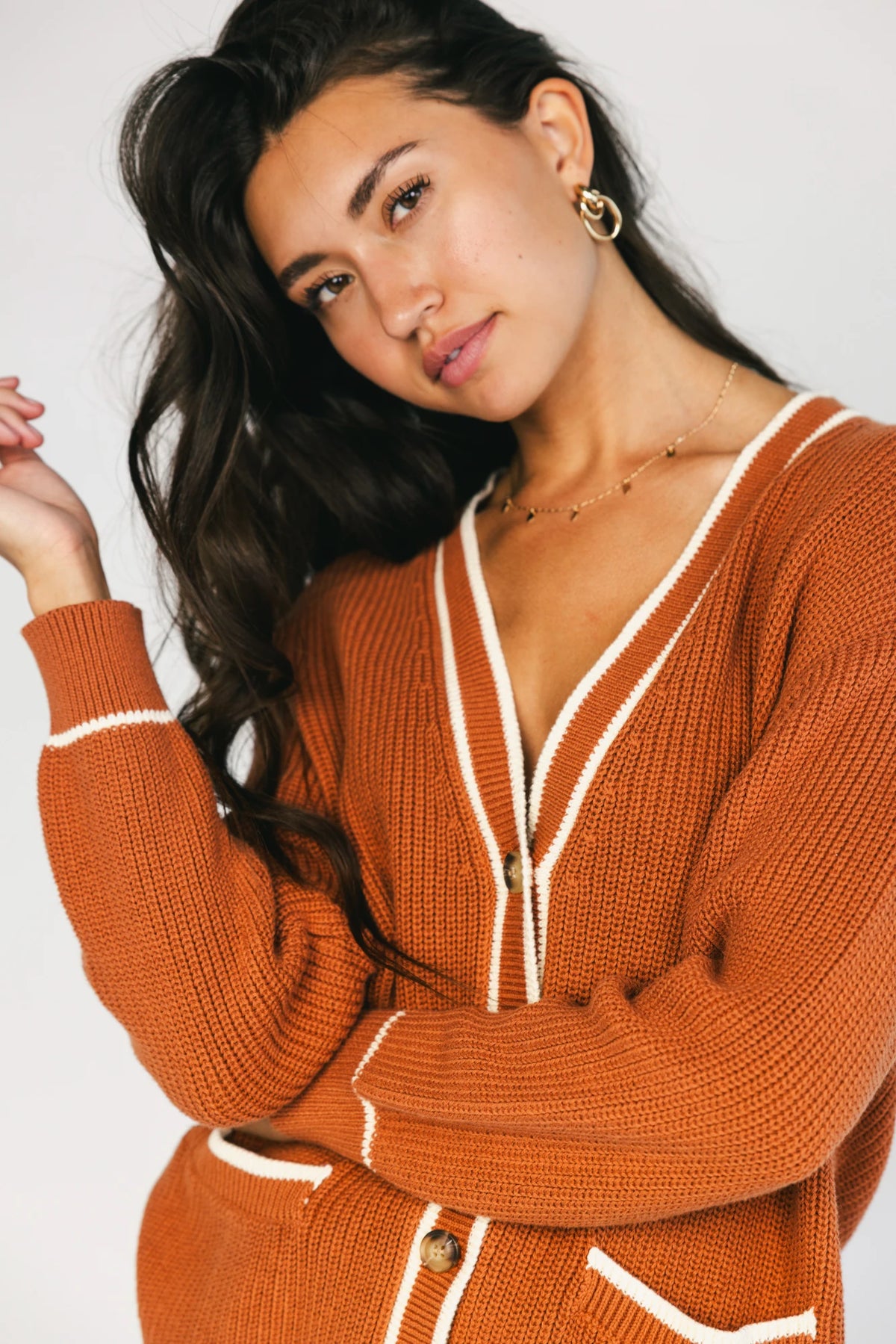 Model wearing a spice orange chunky knit cardigan with a V-neckline, five-button front closure, long sleeves, ribbed trim, front patch pockets, and a relaxed oversized fit.