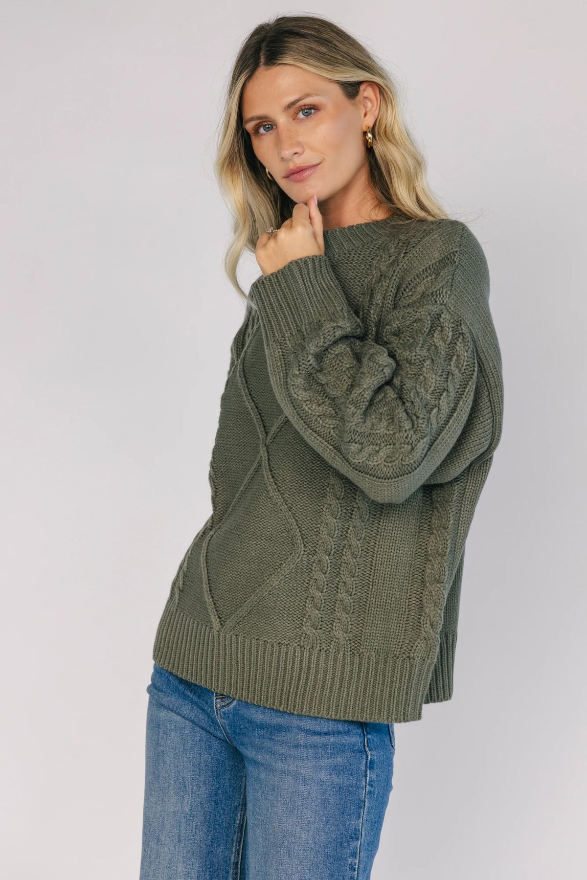 Model wearing an olive knit sweater with a round neckline, long drop-shoulder sleeves, and ribbed trim at the neckline, cuffs, and hem.
