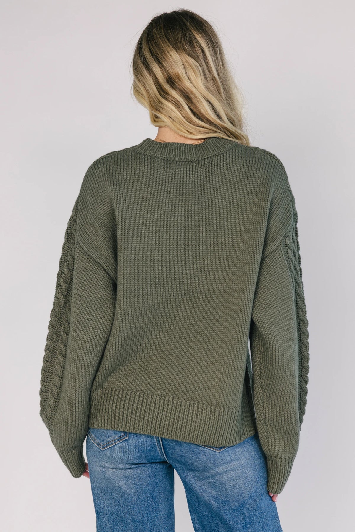 Model wearing an olive knit sweater with a round neckline, long drop-shoulder sleeves, and ribbed trim at the neckline, cuffs, and hem.