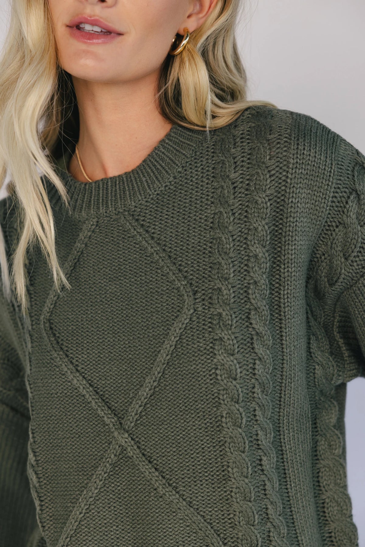 Model wearing an olive knit sweater with a round neckline, long drop-shoulder sleeves, and ribbed trim at the neckline, cuffs, and hem.
