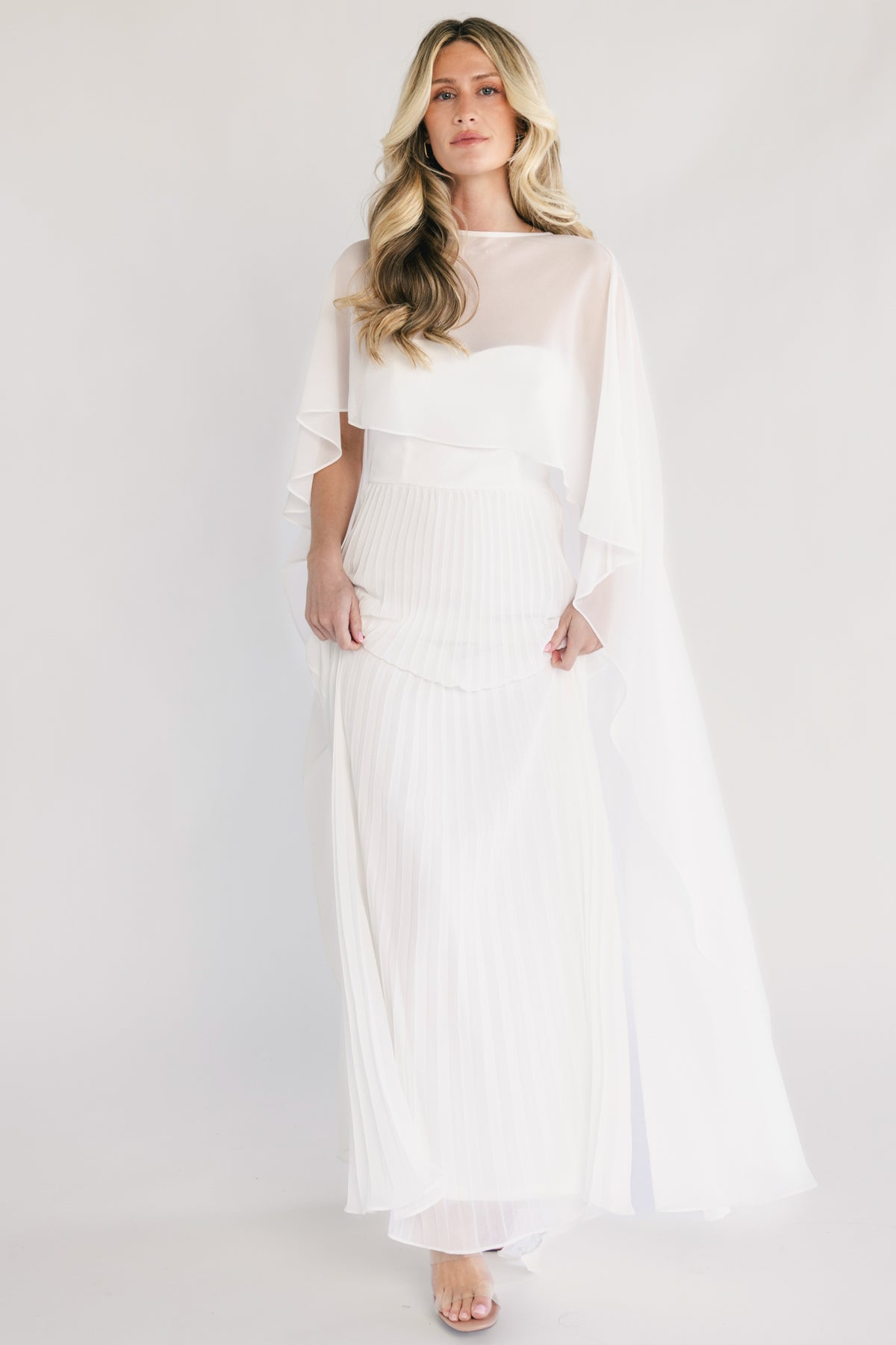 Front view of Serafina strapless sweetheart gown in off white, pleated maxi skirt and removable chiffon cape overlay.
