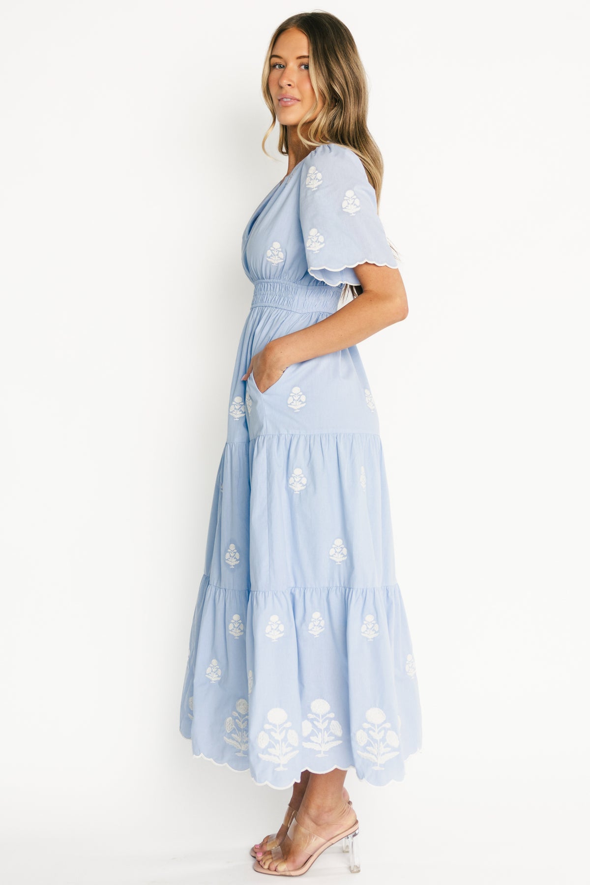 Close-up detail of the Delilah dress embroidery and scalloped sleeve hem in light blue fabric, showing off-white stitched floral motifs and cotton texture.