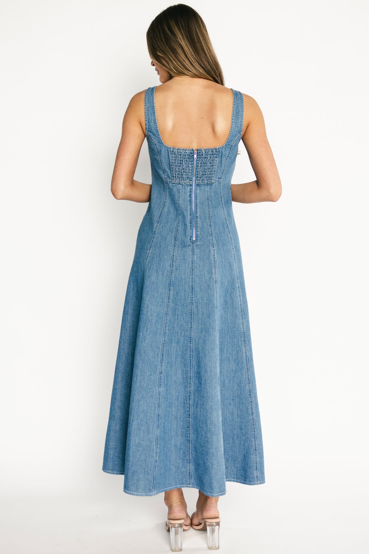 Back view of denim maxi dress highlighting smocked back panel with discreet zipper and unlined 100% cotton construction.