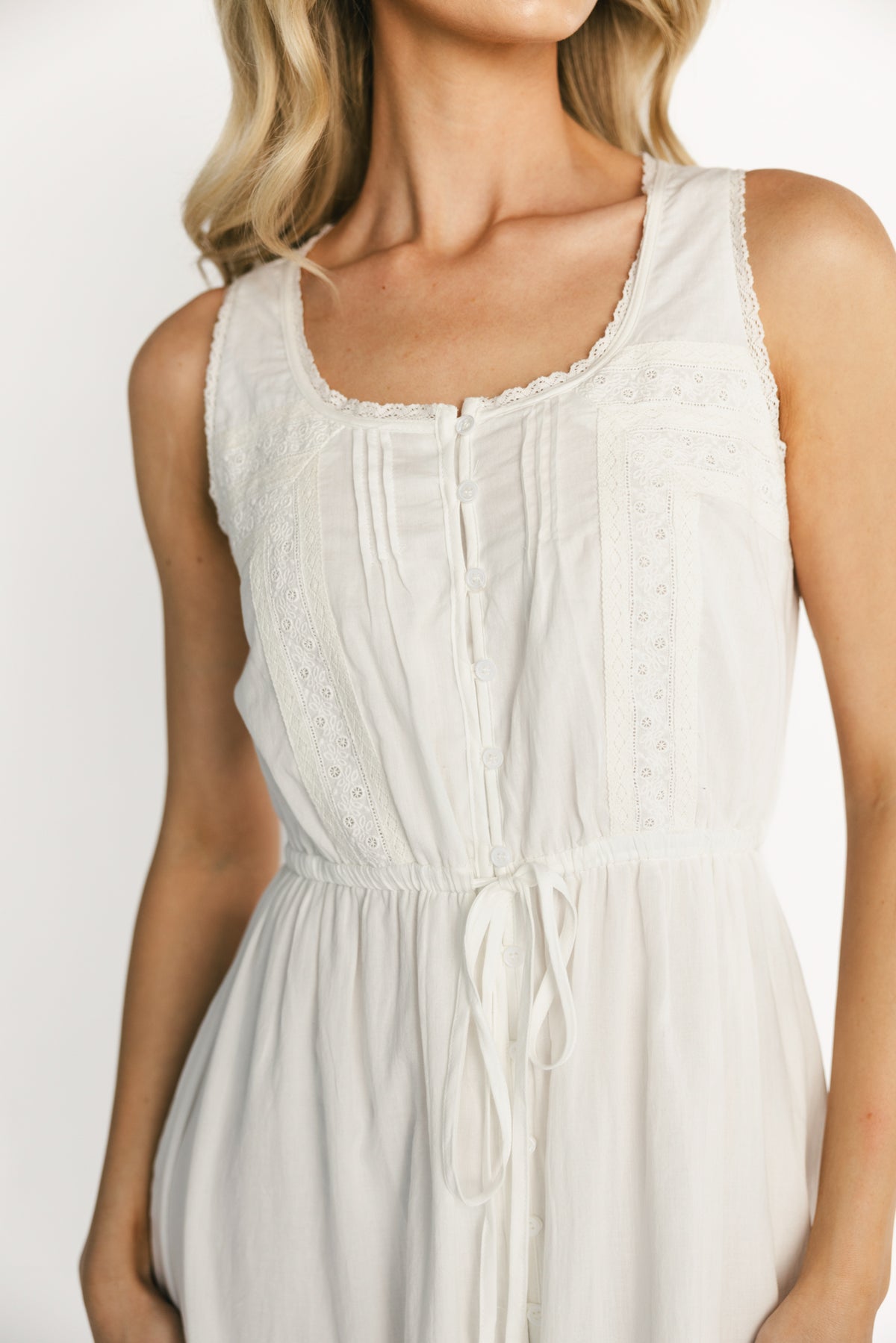 Close-up of bodice showing vertical lace panels, delicate lace trim at the round neckline, and functional wooden-look buttons on off-white cotton.