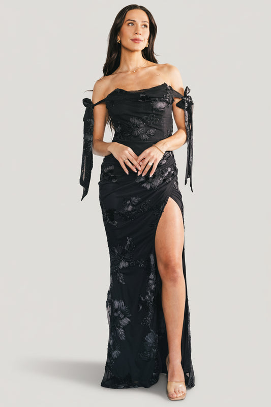 Front view of model wearing the Kinsley off-shoulder black floral maxi dress with cowl neckline and adjustable bow straps for an elegant silhouette.