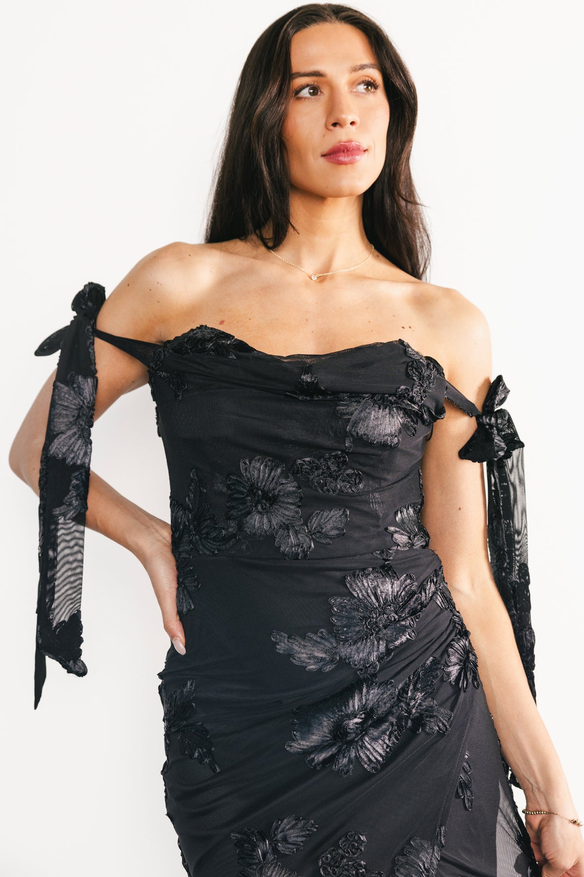 Three-quarter view highlighting black floral appliqué, tulip-style skirt and flowing movement of the Kinsley maxi dress on a styling mannequin.
