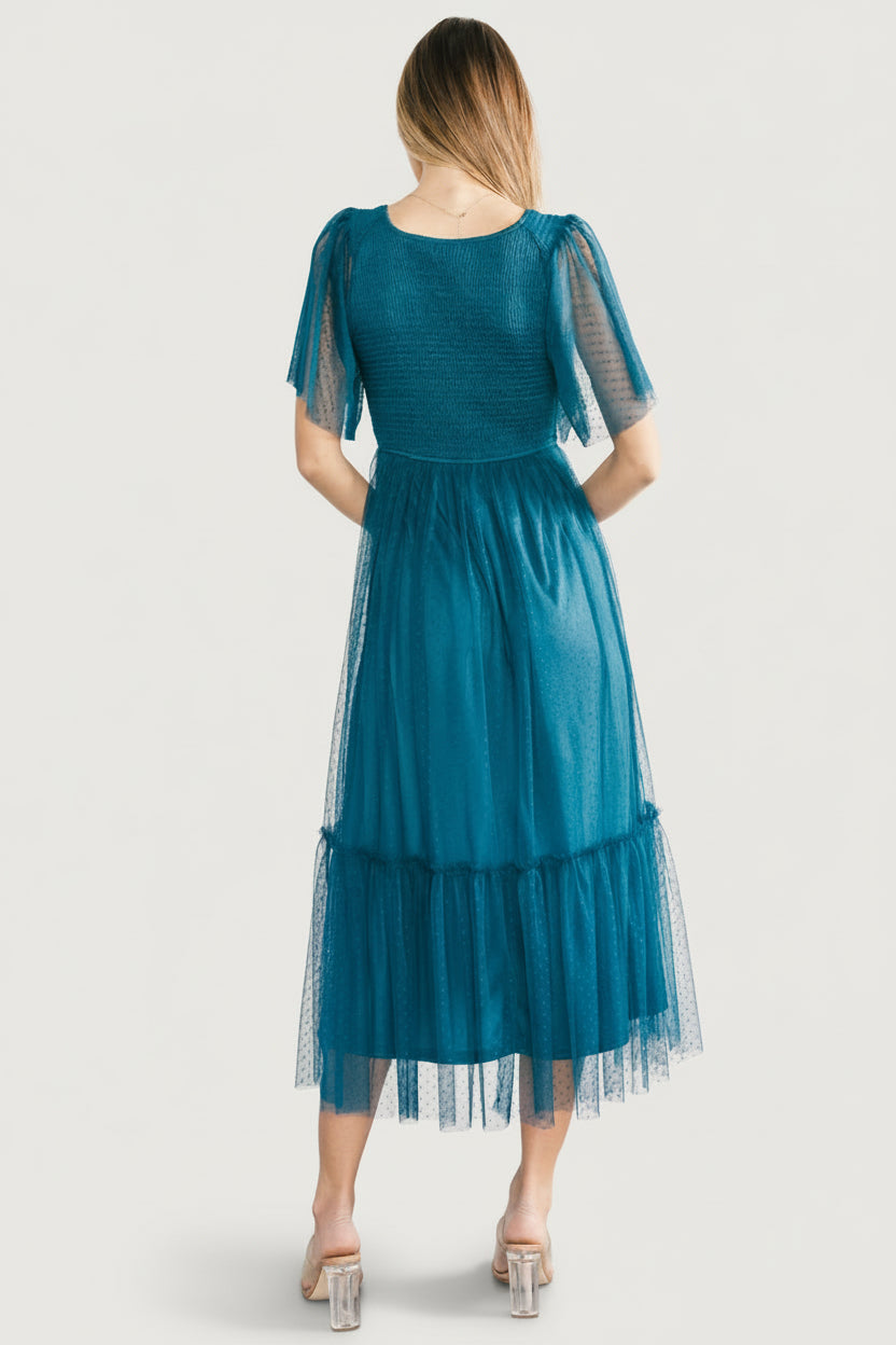 Back view of teal smocked tulle midi dress showing gathered back, tiered ruffled skirt, and lightweight drape of the Swiss-dot overlay.