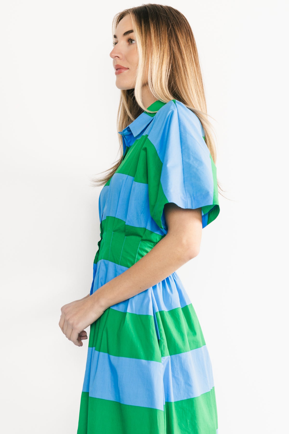Three-quarter side view of the Tracy Shirt Dress showing dolman sleeve drape, hidden side pocket and button-front detail in stripes.