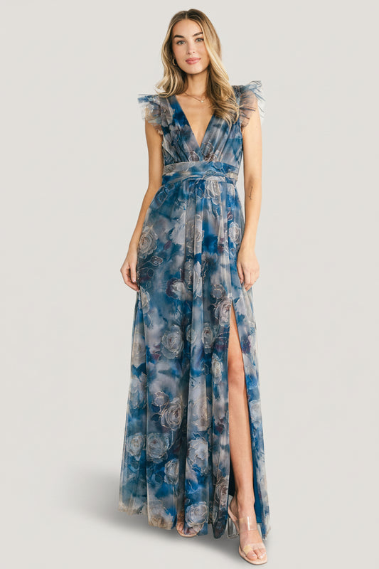 Full-length front view of model wearing Adelyn Maxi Dress in blue floral tulle with deep V-neckline, flutter tank sleeves, banded waist, and left leg slit.