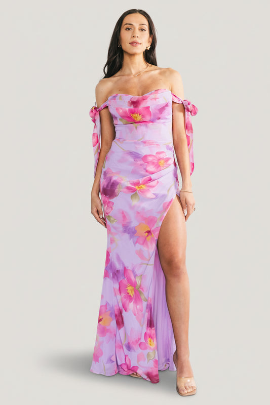 Full-length front view of lavender floral chiffon maxi dress on model, showing off-shoulder bow straps and flowing tulip skirt.