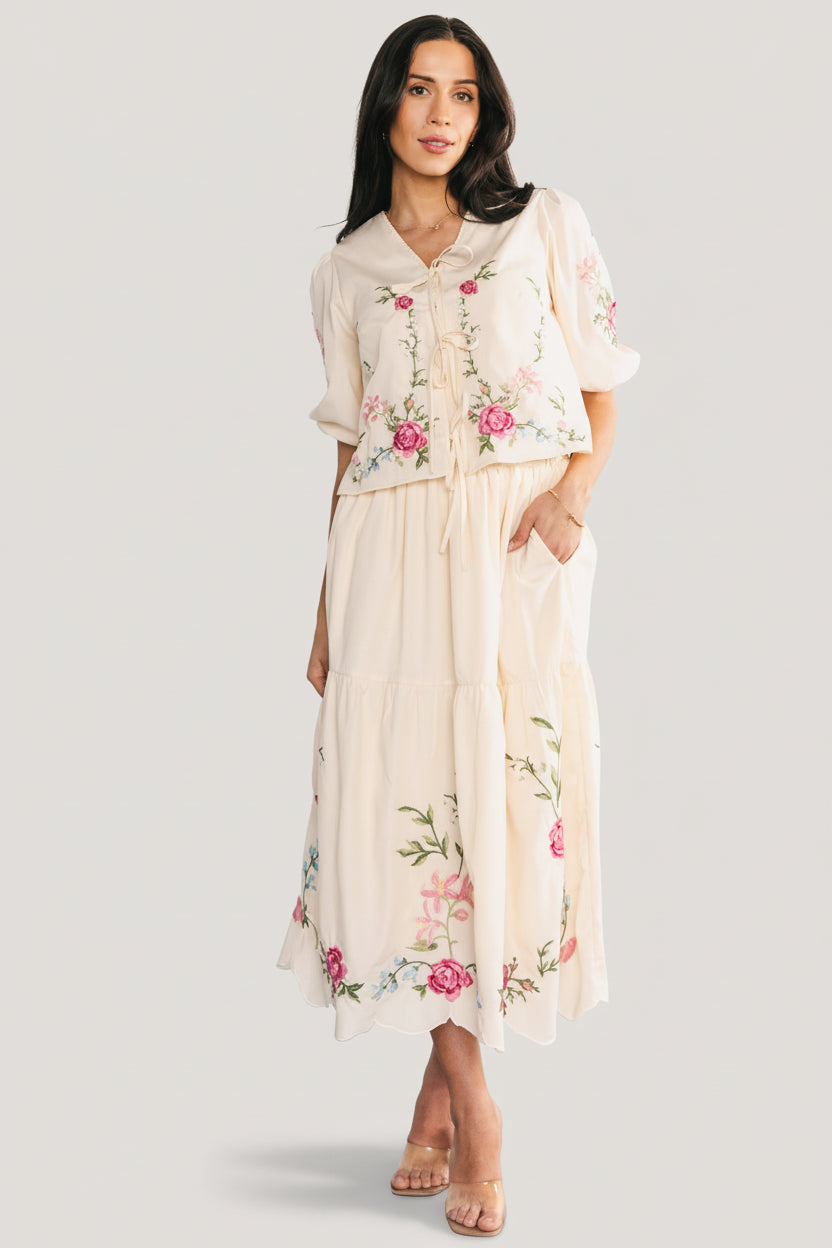 Three-quarter angle showing embroidered detail across the cream top and skirt, scalloped hem of the tiered skirt and elastic back waist.