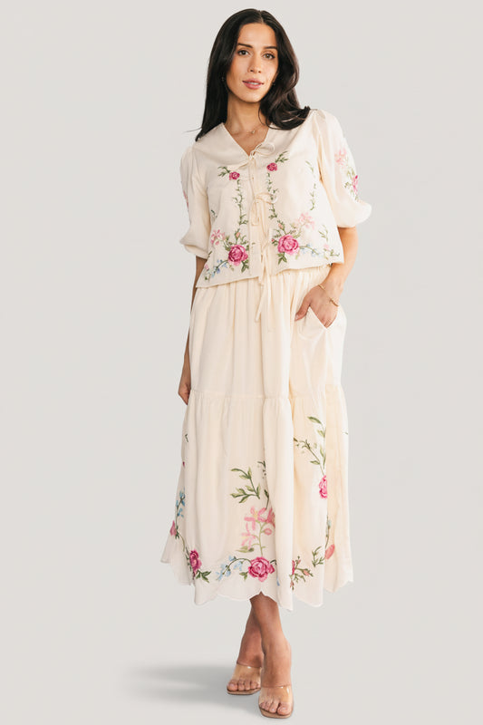 Three-quarter angle showing embroidered detail across the cream top and skirt, scalloped hem of the tiered skirt and elastic back waist.