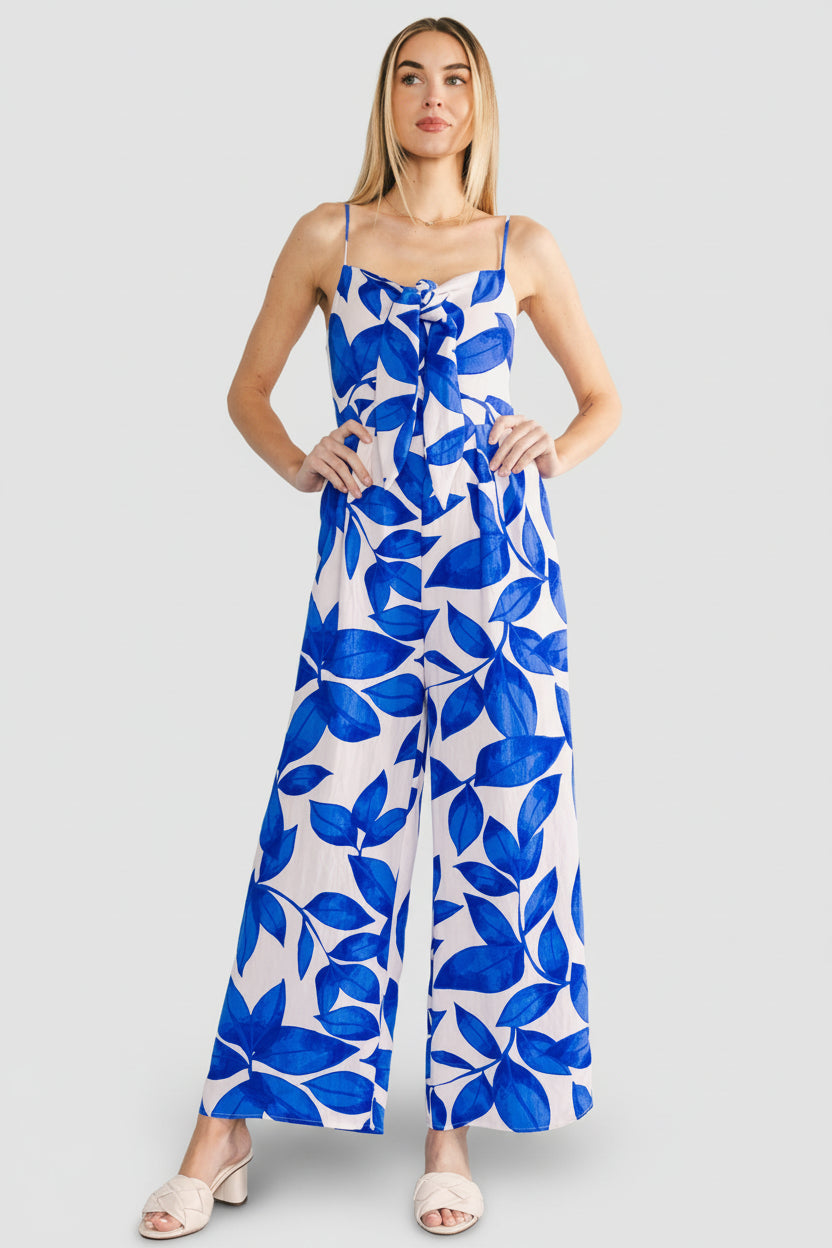 Model wearing Noémie Jumpsuit in cobalt leaf print, angled three-quarter view showing loose straight leg and hidden side pocket detail.