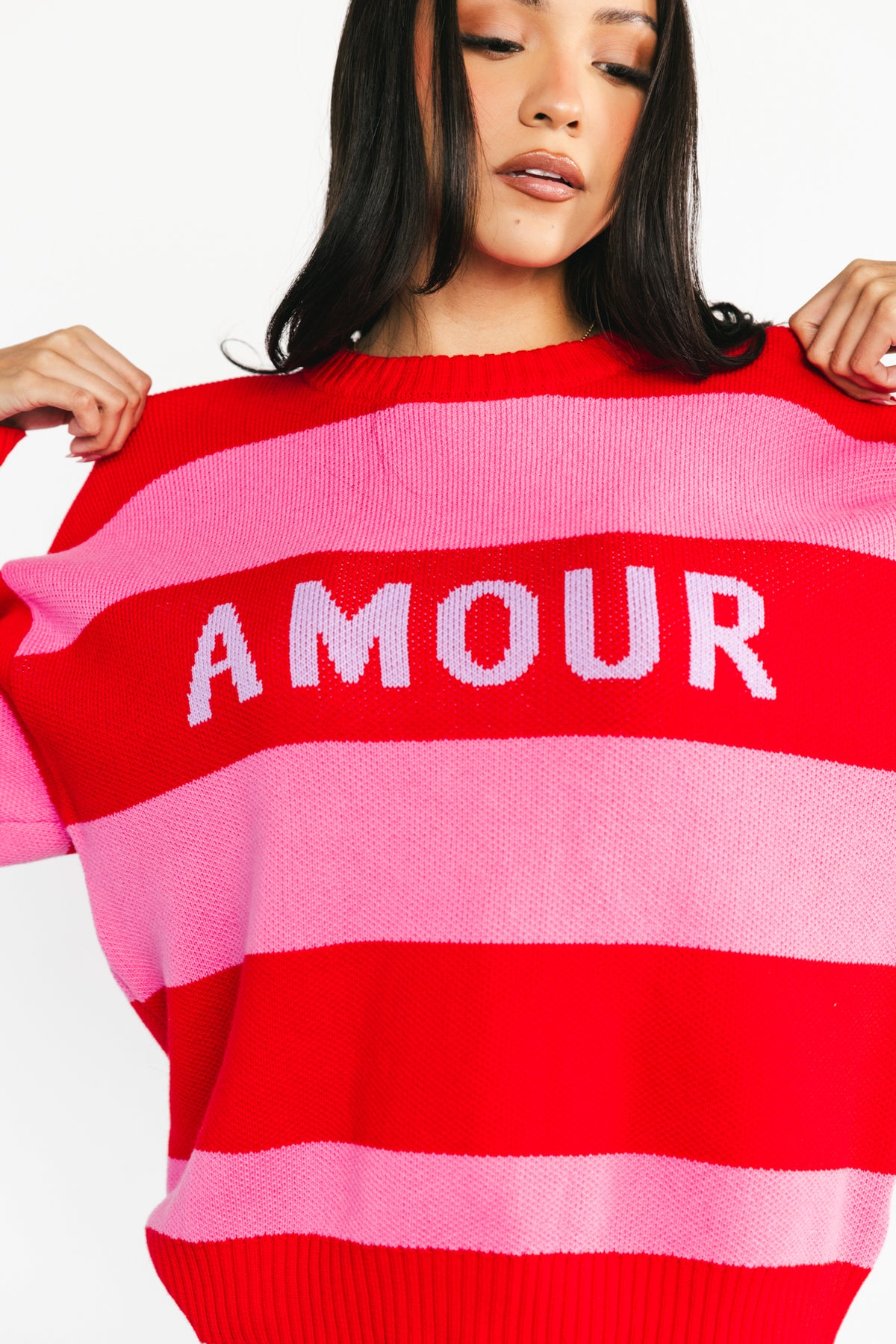 Three-quarter view highlighting the sweater’s oversized silhouette, ribbed hem, and the playful alternating pink and red stripe design.