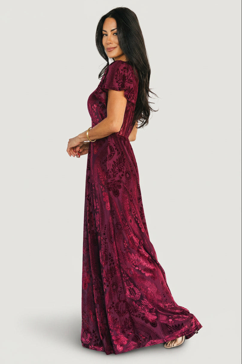 Back view of Kimberly Velvet Maxi Dress in wine revealing flowing maxi hem, subtle burnout mesh floral texture, and unlined sleeves.