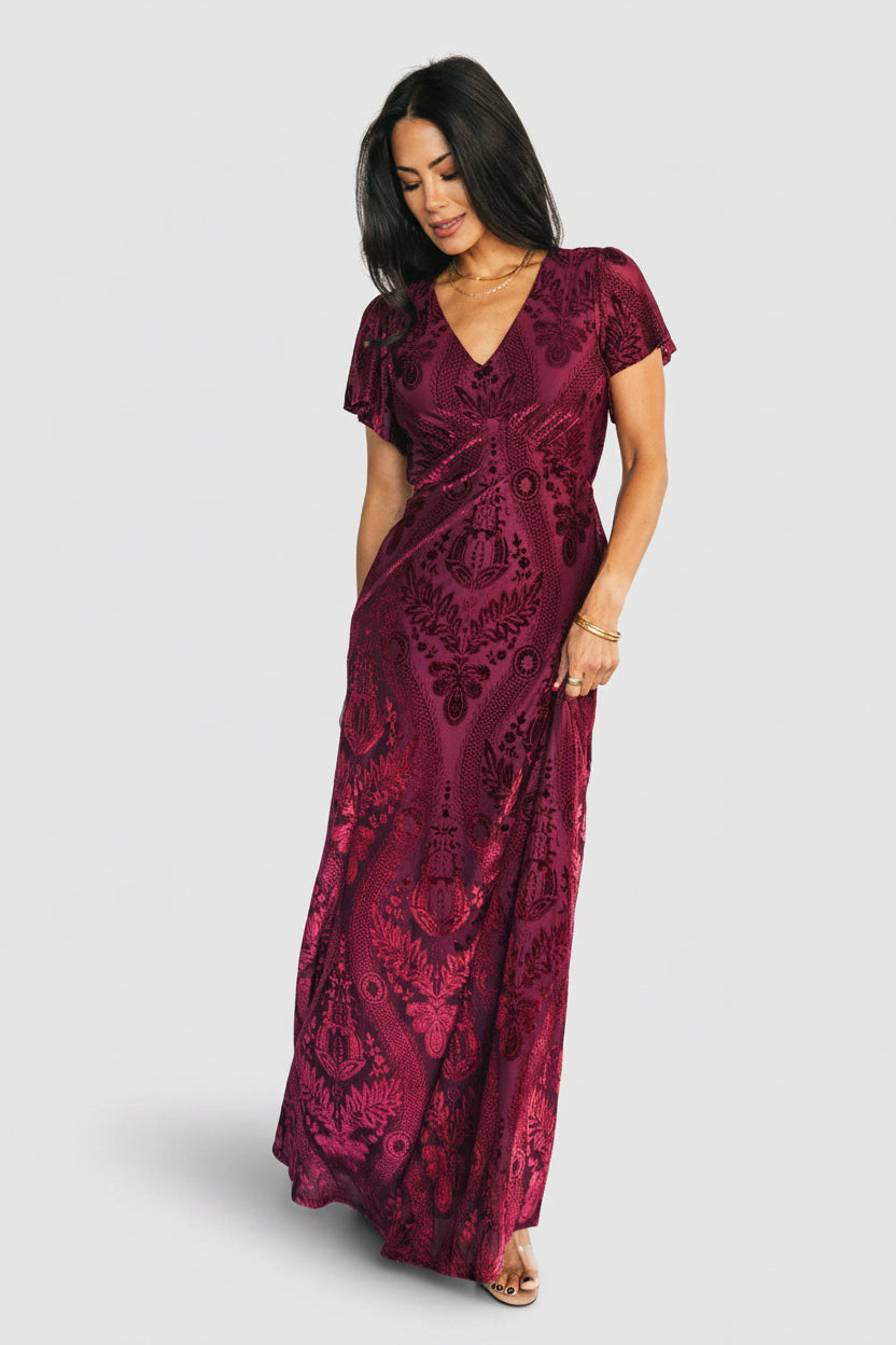 Model walking in Kimberly Velvet Maxi Dress wine, showing skirt movement, V-neck, and flattering empire silhouette for special occasions.