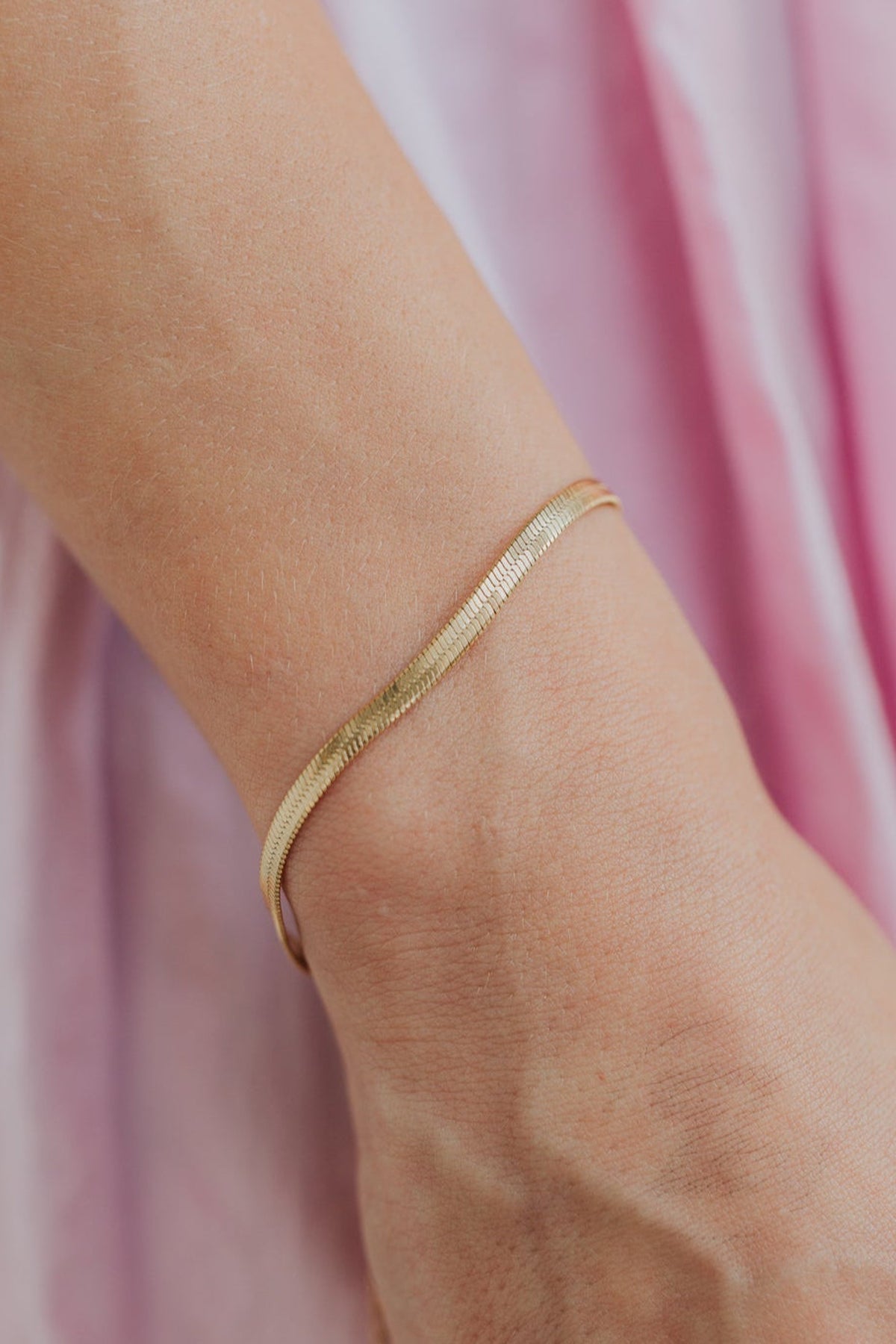 Close-up of the Christina herringbone bracelet showing flat, liquid-like links and high-shine 18K gold plating across the chain.