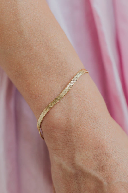 Close-up of the Christina herringbone bracelet showing flat, liquid-like links and high-shine 18K gold plating across the chain.