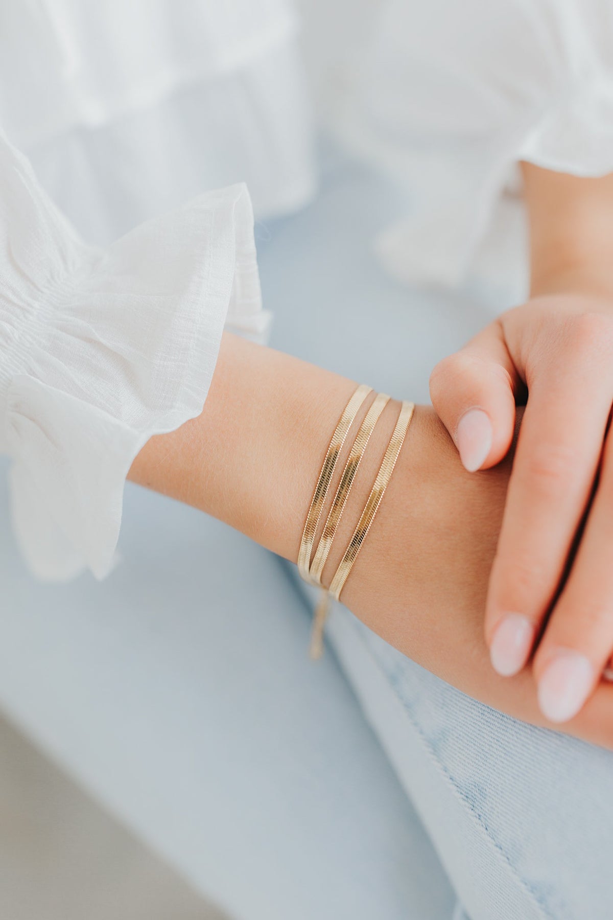 Macro detail of the bracelet links catching light on the high-polish 18K gold finish, showing the flat herringbone construction.