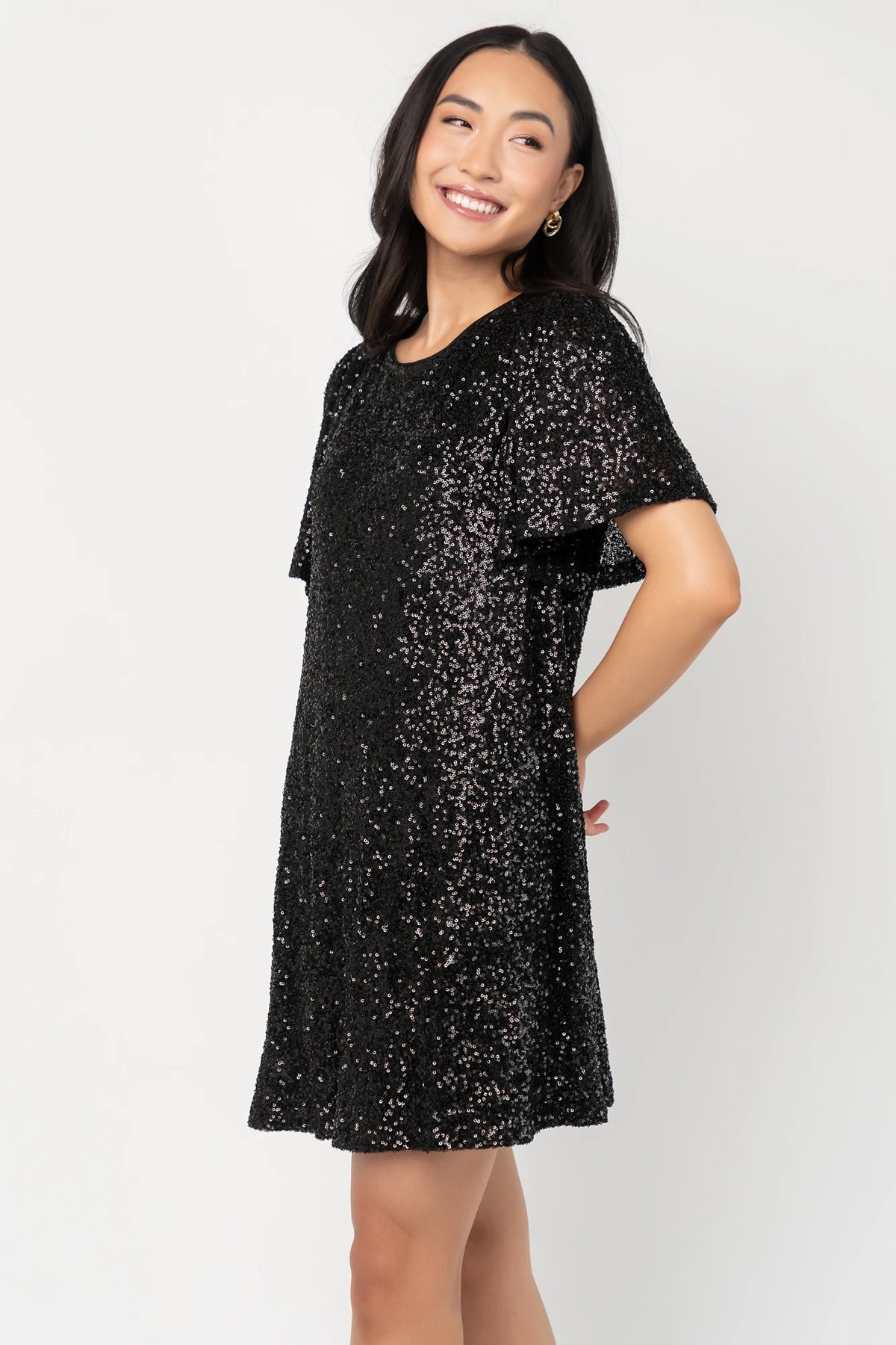 Black liquid sequin mini shift dress with a round neckline, short flutter sleeves, and a satin bow back detail.