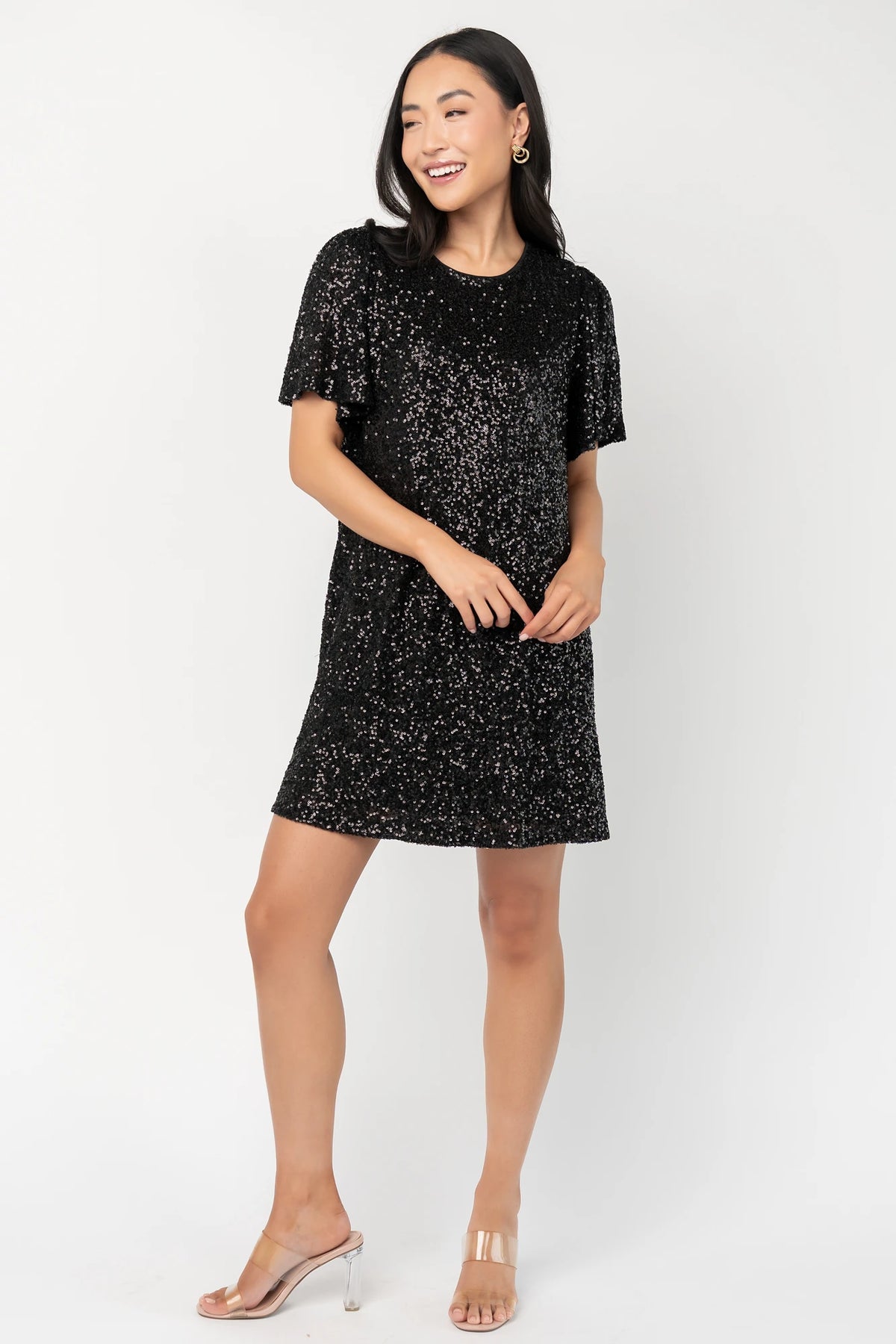 Black liquid sequin mini shift dress with a round neckline, short flutter sleeves, and a satin bow back detail.