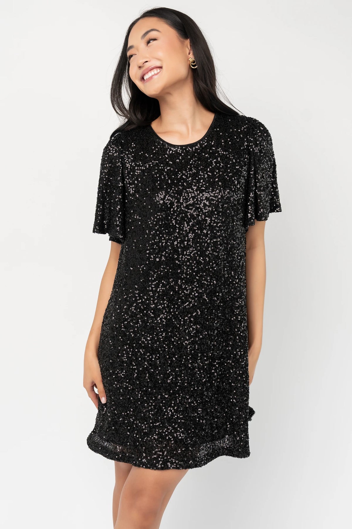 Black liquid sequin mini shift dress with a round neckline, short flutter sleeves, and a satin bow back detail.