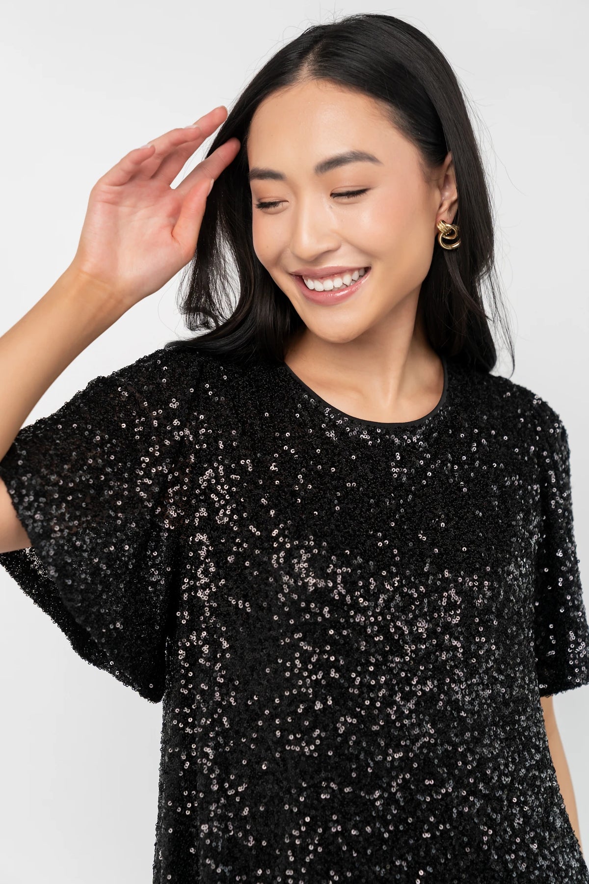 Black liquid sequin mini shift dress with a round neckline, short flutter sleeves, and a satin bow back detail.
