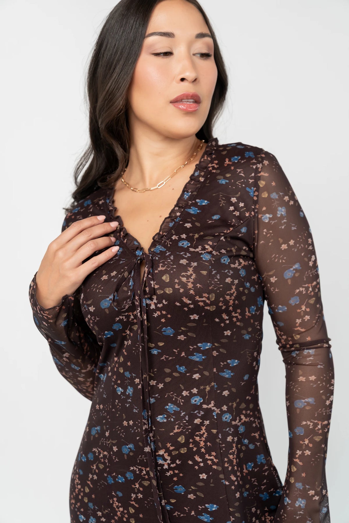 Brown floral mesh maxi dress with blue floral accents, a ruffle-trim V-neckline, adjustable front tie, long sheer sleeves, thigh-high side slit, and a fully lined silhouette.