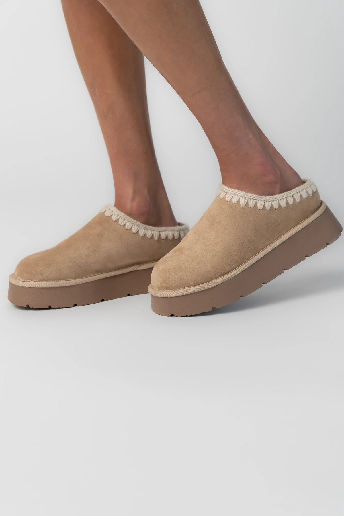 Tan platform mule slippers with a faux suede upper, plush faux fur lining, whipstitch trim, and cushioned slip-on design.