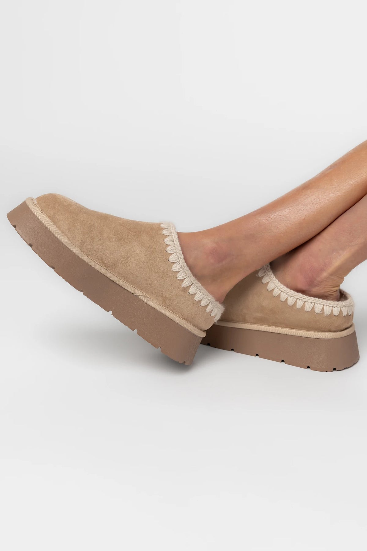 Tan platform mule slippers with a faux suede upper, plush faux fur lining, whipstitch trim, and cushioned slip-on design.