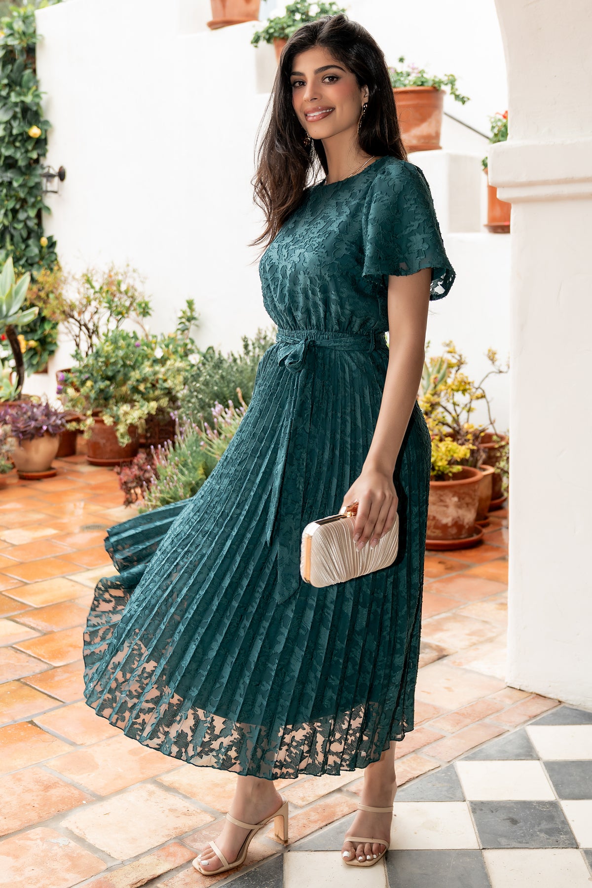 Front view of emerald pleated chiffon dress on model with bloused bodice, flutter sleeves, and detachable sash, studio background.