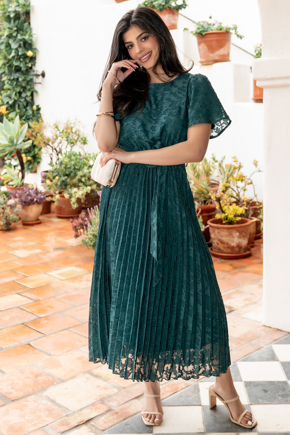 Back view of emerald pleated dress showing single-button keyhole closure and detachable self-tie sash at the natural waist.