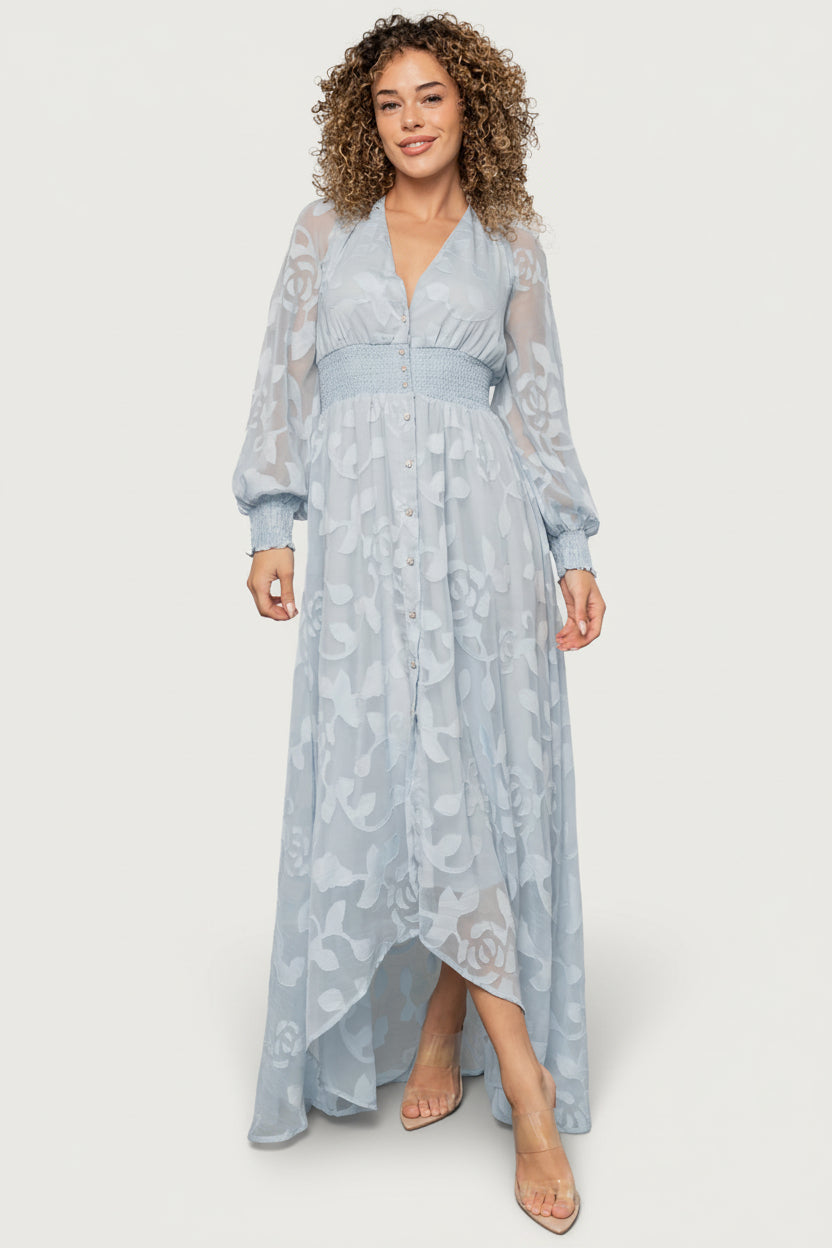 Front view of the Daniella light blue high-low maxi dress in burnout floral chiffon with plunging V-neckline and smocked waistband, styled on a model.