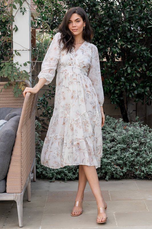 Front view of off-white Raven chiffon midi dress on model, showing surplice neckline, waist ties, and angled tiered skirt in soft floral print.