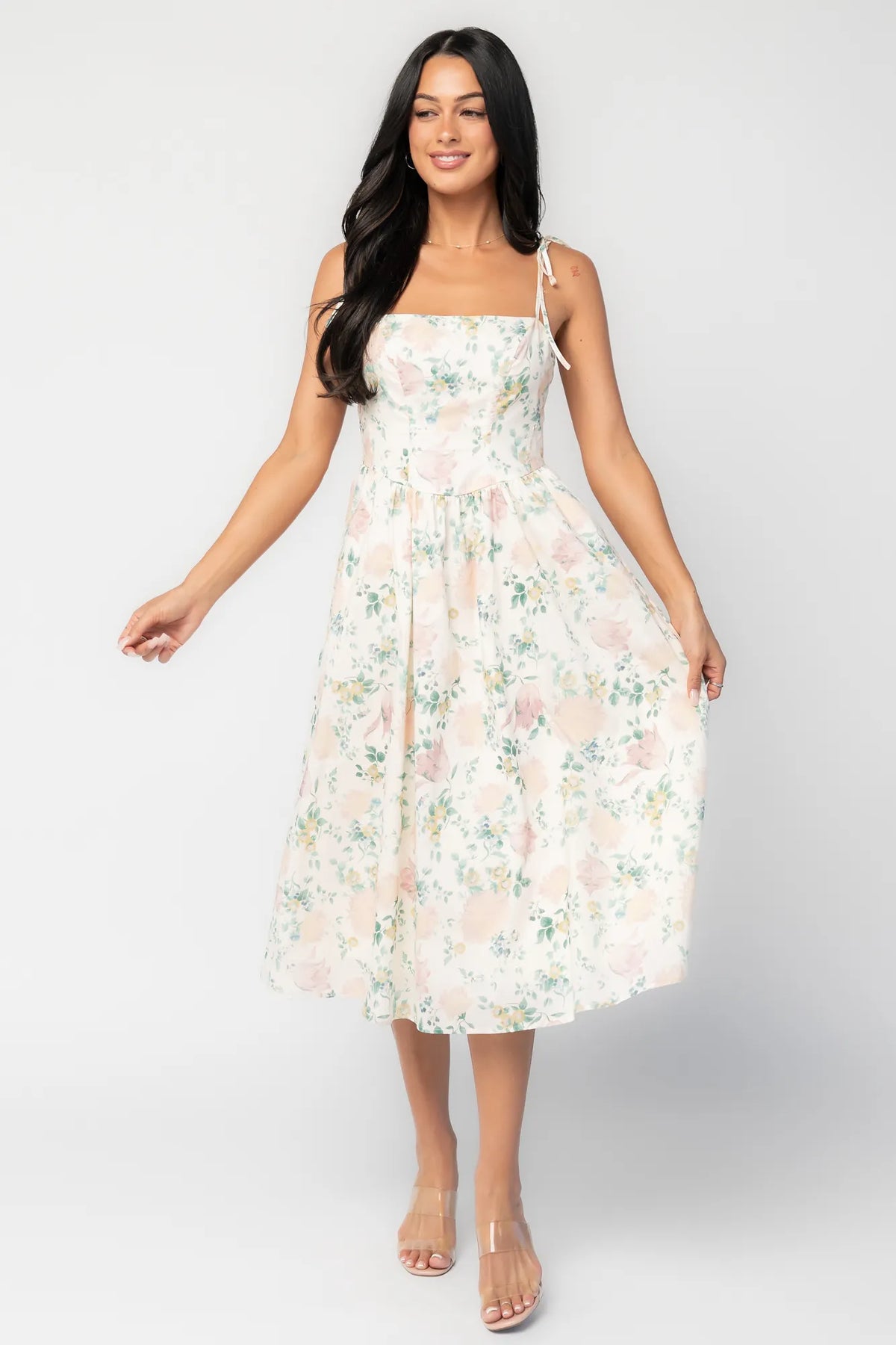 Model wearing a cream floral midi dress with a square neckline, adjustable shoulder tie straps, fitted bodice, and flowing skirt. 