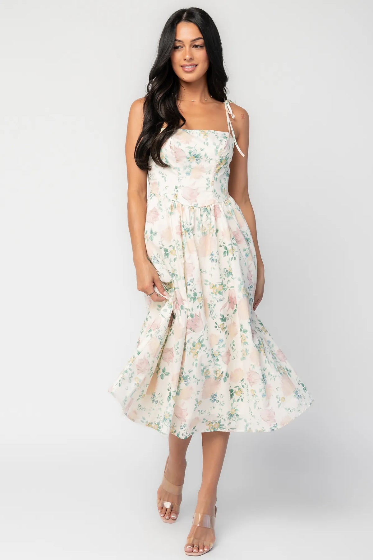 Model wearing a cream floral midi dress with a square neckline, adjustable shoulder tie straps, fitted bodice, and flowing skirt. 