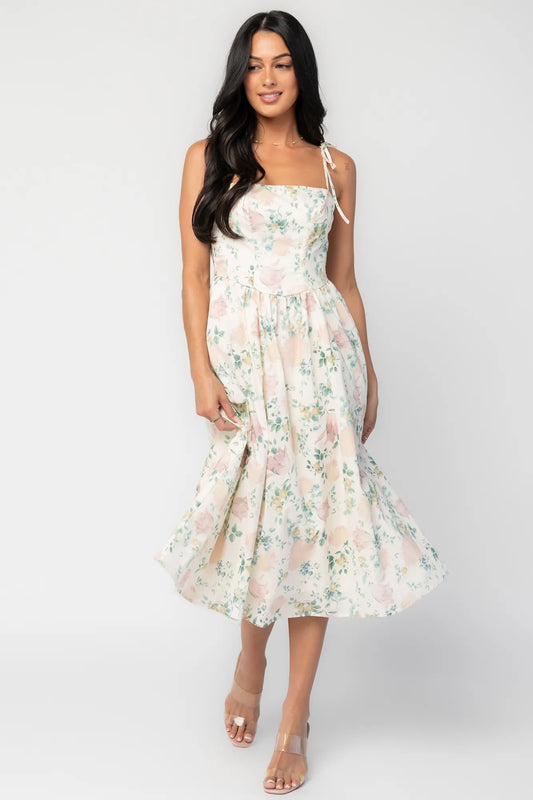 Model wearing a cream floral midi dress with a square neckline, adjustable shoulder tie straps, fitted bodice, and flowing skirt. 