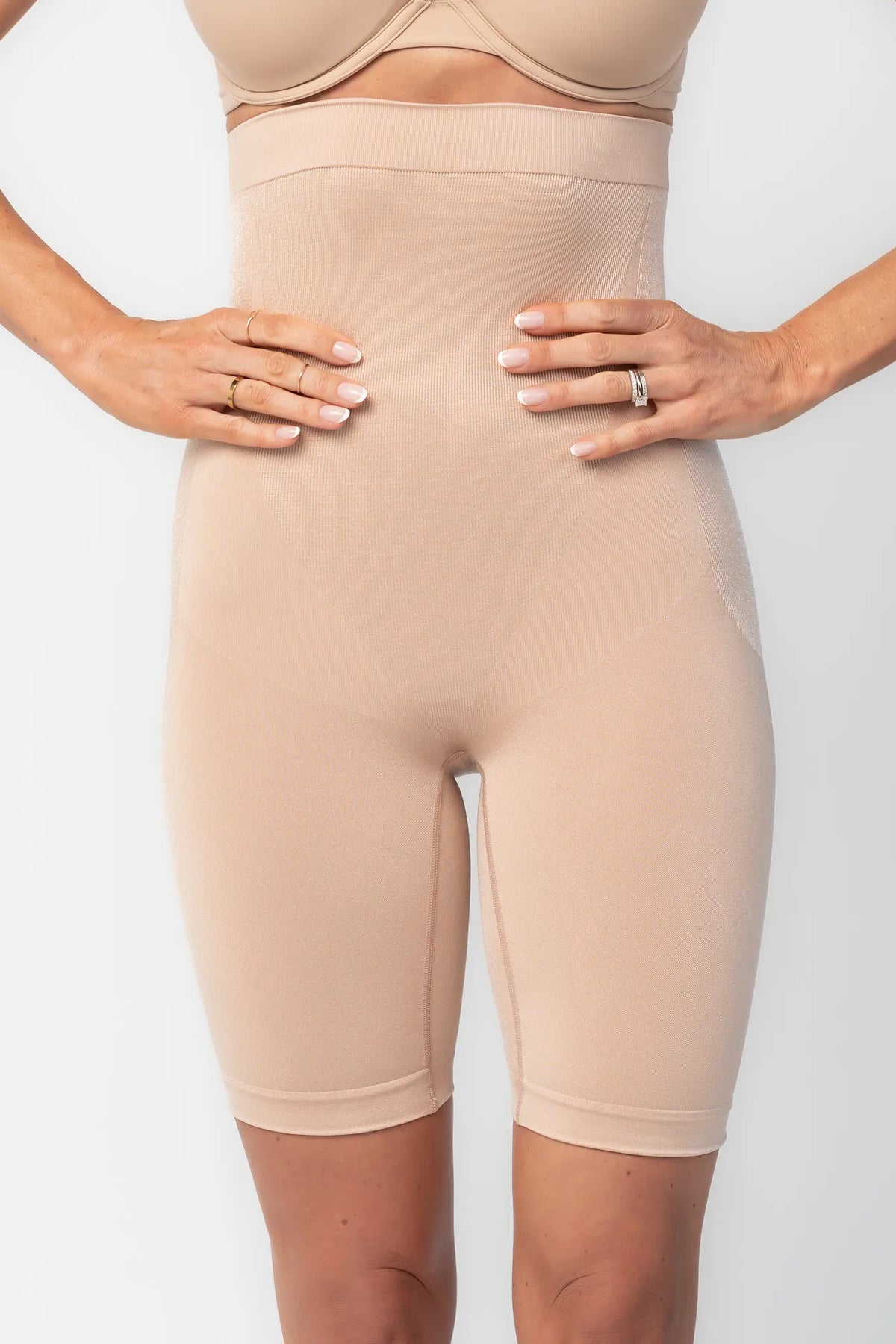 Model wearing nude high-waisted shaping shorts with a seamless design and mid-thigh length.